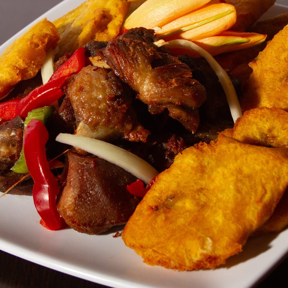 A close-up of Delish Caribbean Restaurant's fried plantains, stewed meat, and colorful bell peppers.