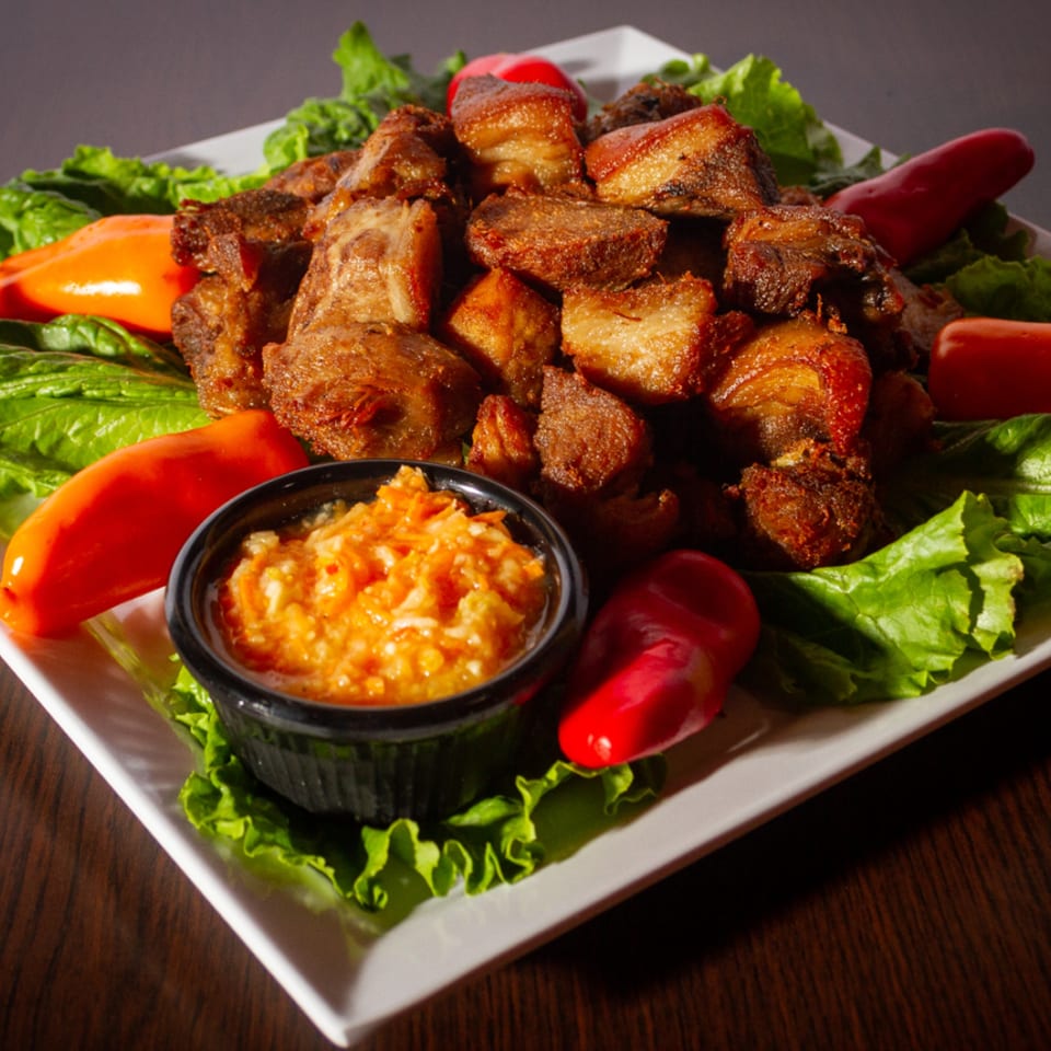 Fried pork chunks with lettuce, sweet peppers, and a side of orange relish on a white plate.