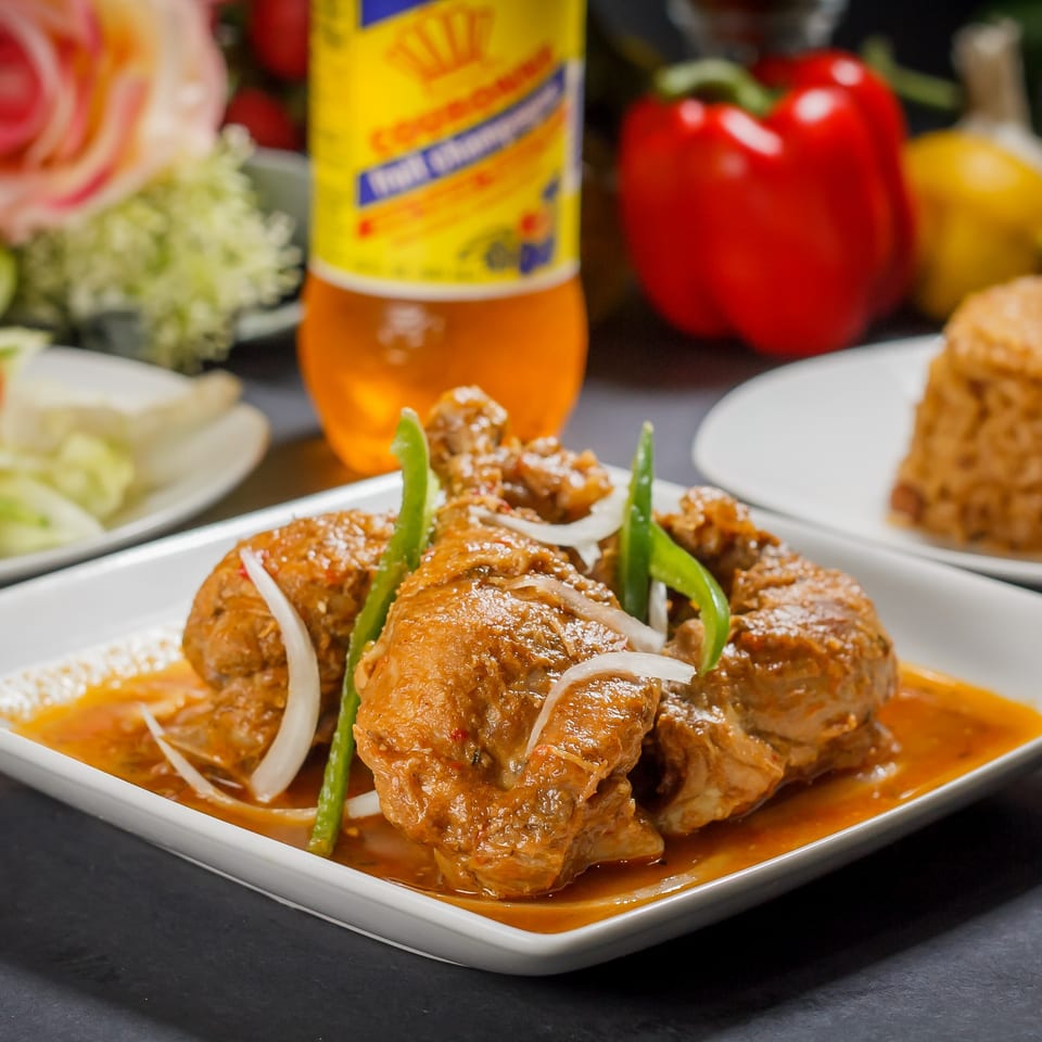 Delish Caribbean Restaurant's stewed chicken with onions and peppers, a drink, and rice.