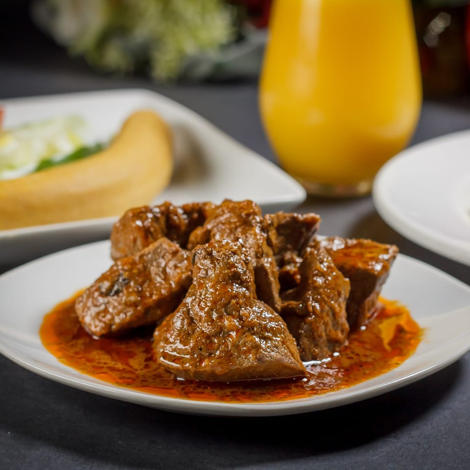 Close-up of Caribbean stewed beef in a rich, reddish-brown sauce on a white plate.